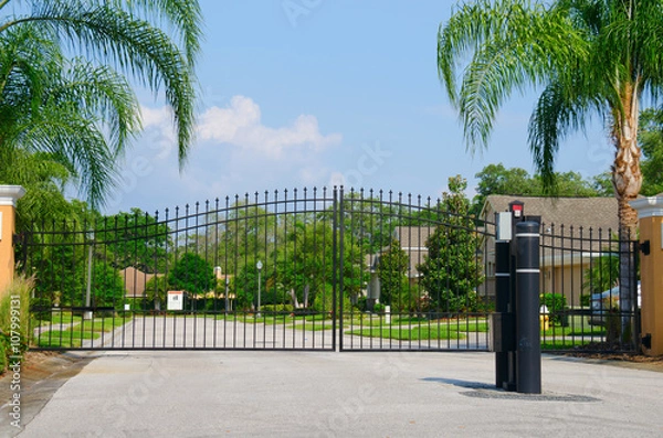 Fototapeta Entrance gate to a beautiful gated residential house community with lush green trees and grass
