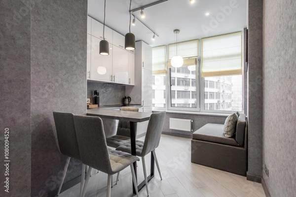 Fototapeta Clean kitchen in a small cozy contemporary studio apartment. Table and chairs in the foreground. Built in household appliance
