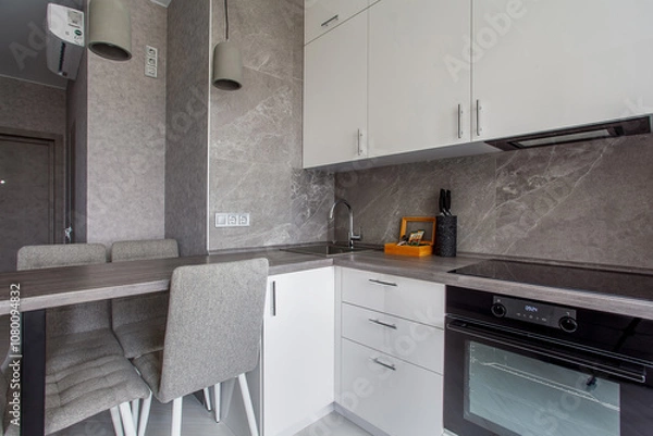 Fototapeta Clean kitchen in a small cozy contemporary studio apartment. Table and chairs in the foreground. Built in household appliance