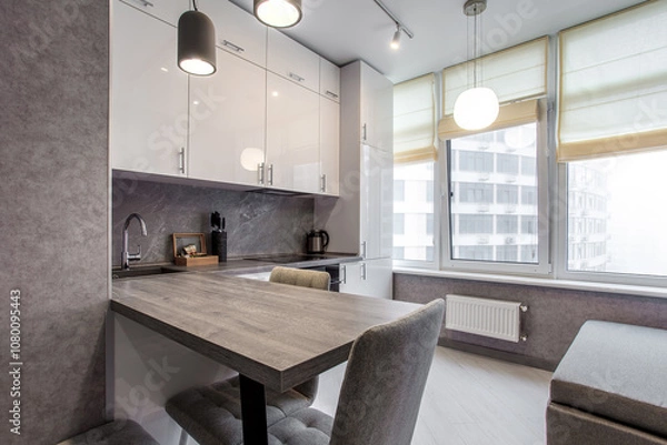 Fototapeta Clean kitchen in a small cozy contemporary studio apartment. Table and chairs in the foreground. Built in household appliance