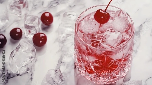 Fototapeta Refreshing cherry cocktail with ice cubes, garnished with a cherry on top, in a stylish glass on a marble surface