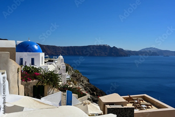 Obraz Eine Panoramaaussicht von Oia auf der griechischen Insel Santorin, zu einer der bekannten blauen Kuppelkirchen und den weiteren verlauf der Caldera bis nach Fira.