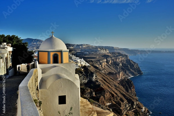 Obraz Die Kirche Agios Stylionos auf der Griechischen Insel Santorin steht direkt an der Caldera bei der Stadt Fira. Man sieht schön der verlauf der steilen Abbruchkante der Caldera im warmen Abendlicht.