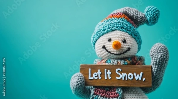 Fototapeta Smiling crochet snowman holding let it snow sign on turquoise background