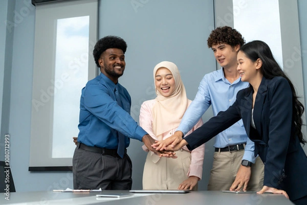 Obraz Cheerful group of professionals stacking hands in a workplace, symbolizing unity, collaboration, and successful teamwork in a diverse setting.