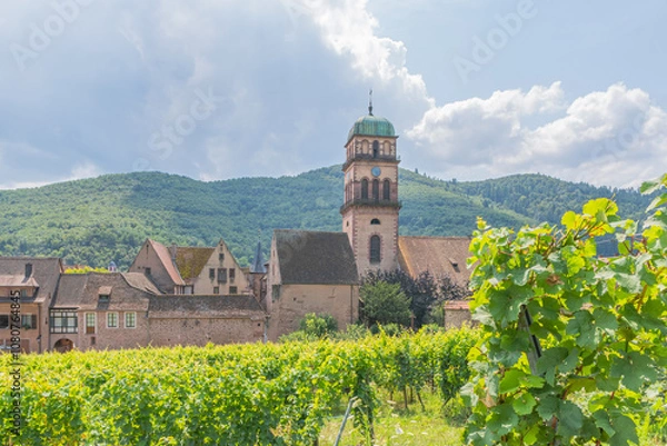 Fototapeta Eglise de Kaysersberg au milieu des feuilles de vignes, village coloré sur la route des vins d'Alsace, France.