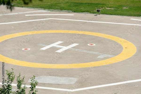 Fototapeta A closeup of an asphalt-covered helipad with a special symbol in the center for helicopter landing.  Helipad in the park.