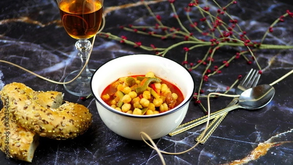 Fototapeta Dish with chickpeas, peppers, carrots and other vegetables with a whole grain roll and a glass of wine

