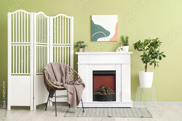 Fototapeta White fireplace, houseplants, armchair and folding screen in interior of stylish living room
