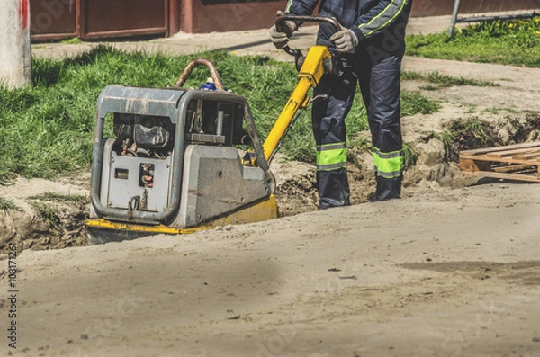 Obraz A worker with a vibrating plate in a ditch