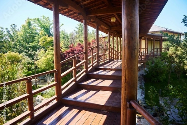 Fototapeta A wooden walkway with a view of the trees and the bridge. The walkway is connected by wooden posts and has a wooden railing