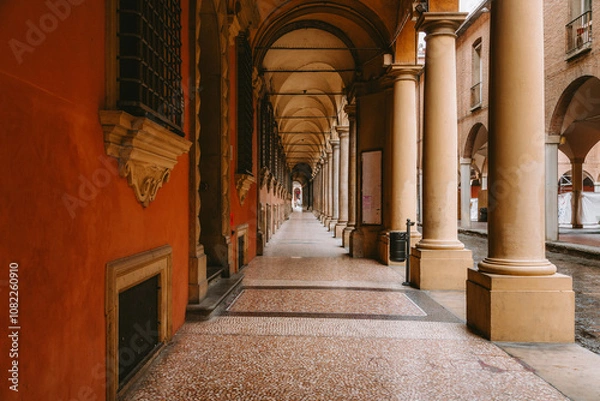 Obraz Warm sunlight illuminates the long, empty colonnade with its repetitive arches and columns, creating a striking perspective and highlighting the architectural beauty of bologna