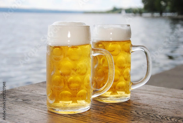 Obraz Kühles, frische Bier / Zwei Bierkrüge mit frischem Bier draußen am See  