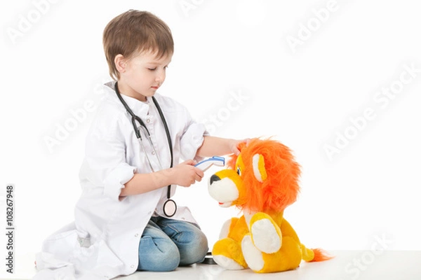 Fototapeta Baby boy in a white robe doctor mereet body temperature of the device at the cub toy . Isolated on white background