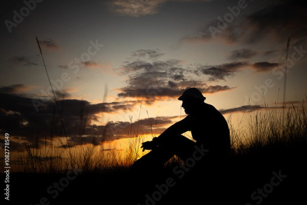Obraz Silhouette eines Mannes der auf einer Wiese bei Sonnenuntergang sitzt