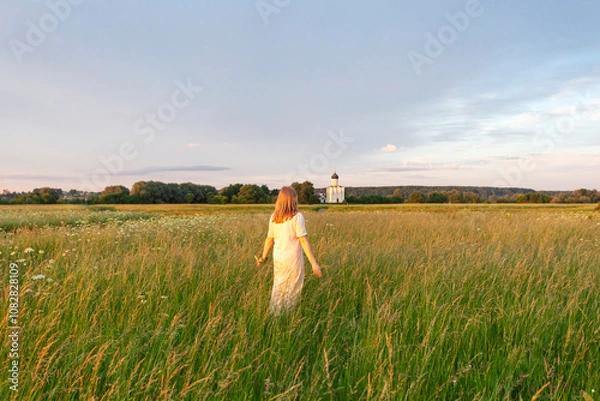 Fototapeta A white long-haired girl walks through a blooming meadow