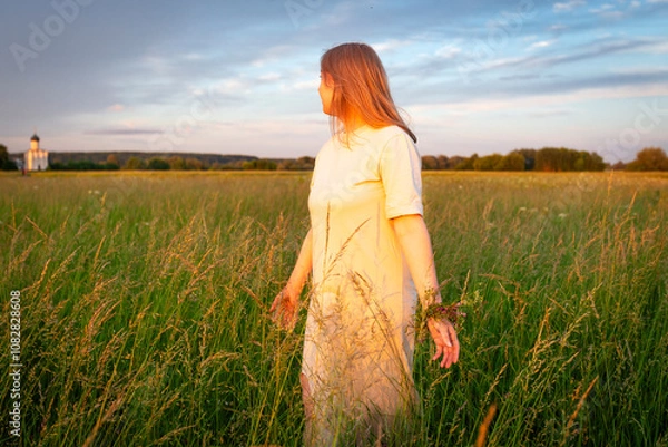 Fototapeta A white long-haired girl walks through a blooming meadow