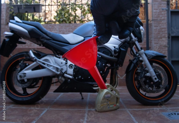 Fototapeta A hand with black latex gloves, holding a funnel to change the engine oil of a motorcycle. A motorcycle in the background. Maintenance concept.