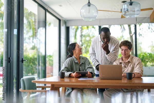 Fototapeta A cheerful diverse group of young adult professionals engage in a discussion over a laptop, dressed in casual business attire, in a bright and modern office environment.