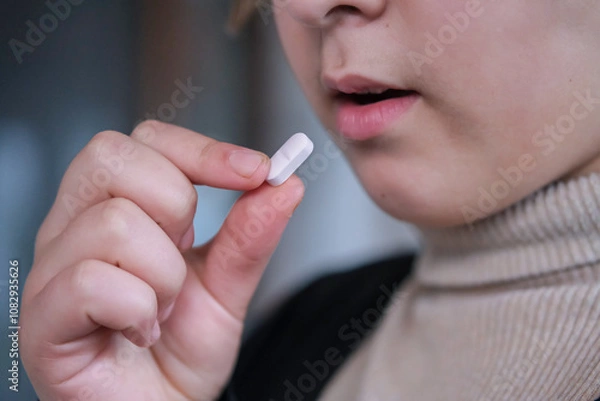 Fototapeta Close up image of a girl  taking white round pill. Young girl taking medicines, antidepressant.