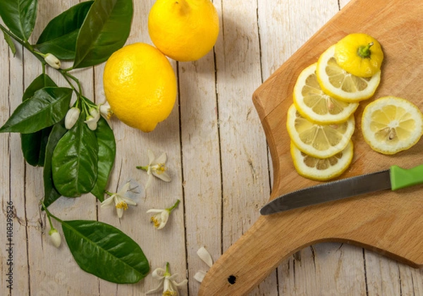 Obraz Несколько спелых лимонов украшенных листьями цветущего лимонного дерева на деревянном фоне