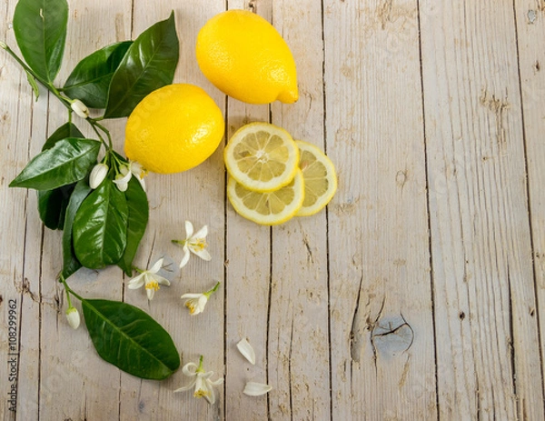 Obraz Несколько спелых лимонов украшенных листьями цветущего лимонного дерева на деревянном фоне