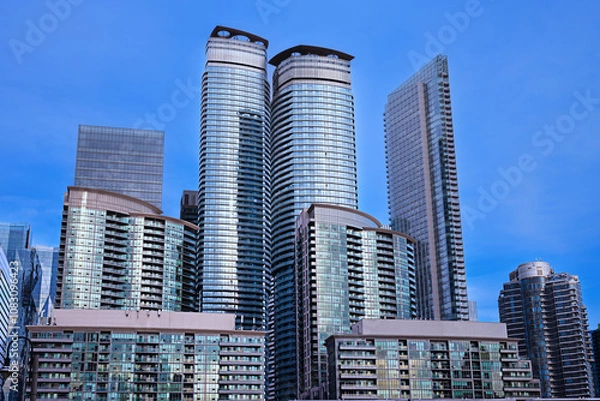 Obraz Modern high-rise buildings against a clear blue sky. Primarily with reflective surfaces that mirror the sky and surrounding structures. 