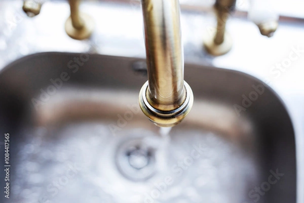 Obraz Gold running tap with water falling into silver metal sink 
