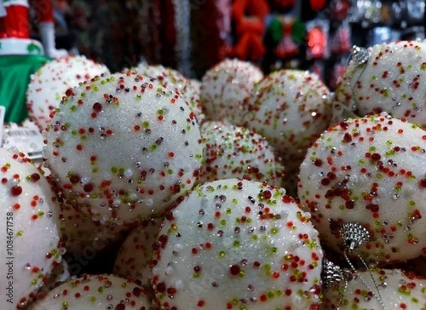 Fototapeta White colored Christmas baubles  with green and red speckles are on a store shelf during a Christmas show in a shop and are ready to be sold before the start of the holiday season