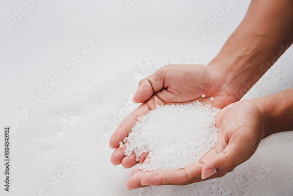 Fototapeta Hands hold clear white plastic pellets, raw materials for various manufacturing processes. These pellets are widely used in industries to produce products like packaging, bottles, and equipment parts.