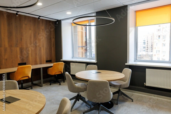 Fototapeta Empty working and meeting area in an open office. White round wooden table surrounded by chairs in grey and yellow colors. Big window background
