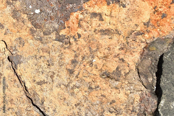 Fototapeta Weathered stone surface with rough texture and peeling layers. Grunge rock wall background with natural erosion patterns. Old cracked stone texture showing age and decay
