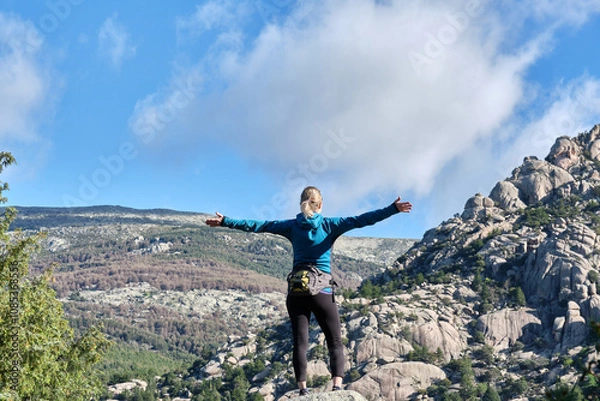 Obraz A hiker woman standing with hands raised looking at mountains in the Sierra de Guadarrama National Park.