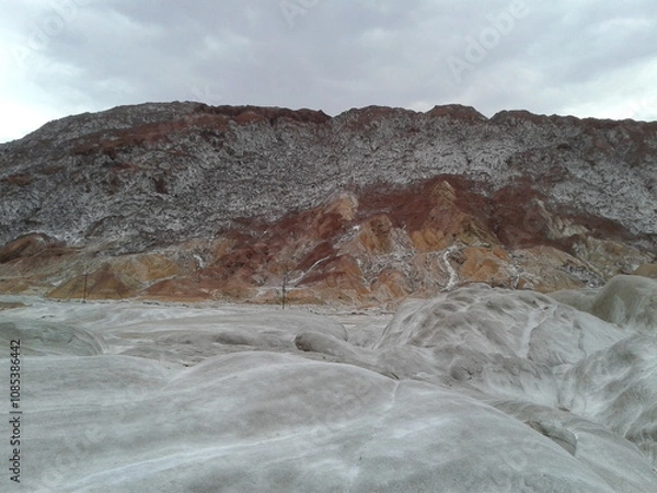 Fototapeta A stunning view of a rocky mountain surrounded by salt formations, showcasing unique natural textures and colors under a serene sky.