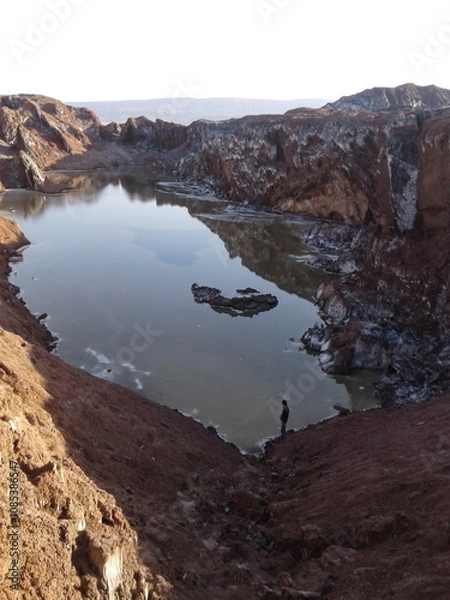 Fototapeta A natural pond surrounded by rocky cliffs, creating a contrast between water and dry terrain, highlighting the beauty of rare oases.