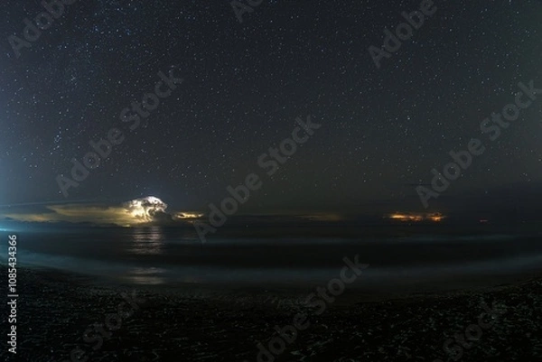 Fototapeta Thunderstorm cell over the sea at night with visible stars in the sky, creating a dramatic scene