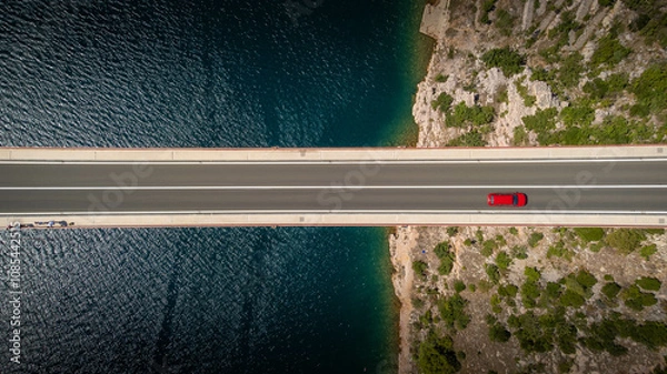Obraz Top down view of a red car alone driving on a bridge over the sea. Background images for travel, holidays, the beauty of traveling by car to discover a country. Maslenica bridge, Croatia.