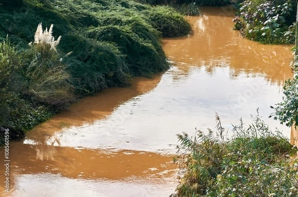 Fototapeta Stream of dirty water flowing vigorously after heavy rainfall. The murky appearance indicates a high content of sediment and pollutants, showing the effects of natural runoff.