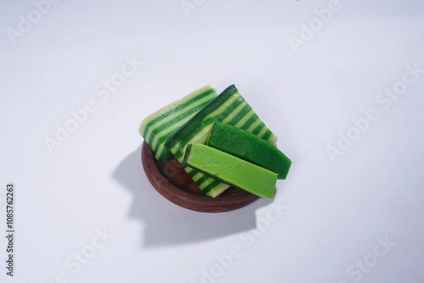 Obraz Sticky layer cake or Kue Lapis on wooden plate isolated on white background. Indonesian traditional dessert made from rice flour and coconut milk, steamed layer by layer served on banana leaves. Selec