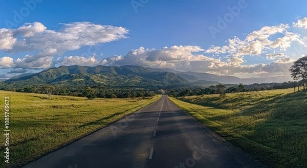 Obraz wide road leads into the distance, with green mountains and a blue sky in the background