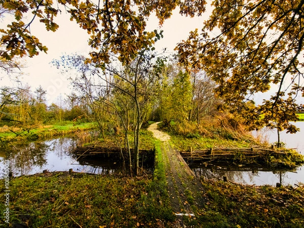 Fototapeta Dutch polder landscape with peat quay Spookverlaat at Kruiskade, Hazerswoude-Rijndijk and ditch with wooden footbridge in shell path seen from west to east during sunrise
