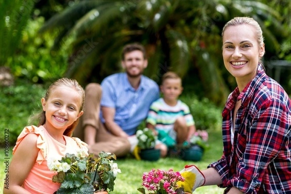 Fototapeta Smiling mother and daughter with flower pots in yard 