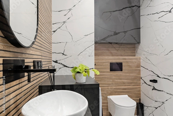 Fototapeta Modern interior of bathroom with ceramic wash basin with black faucet and brown striped tiles on the wall and circle mirror. Luxurious hygiene room in industrial style. Elegant home.