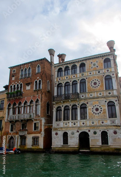 Fototapeta A view of historic Venetian buildings along the Grand Canal, showcasing classic Italian architecture. The iconic canal waters reflect the facades, with boats and gondolas adding to the charm of Venice