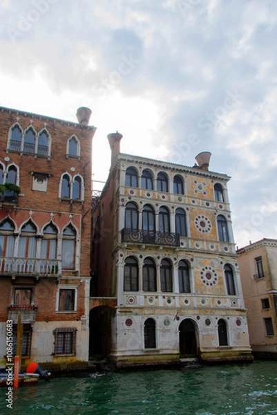 Fototapeta A view of historic Venetian buildings along the Grand Canal, showcasing classic Italian architecture. The iconic canal waters reflect the facades, with boats and gondolas adding to the charm of Venice