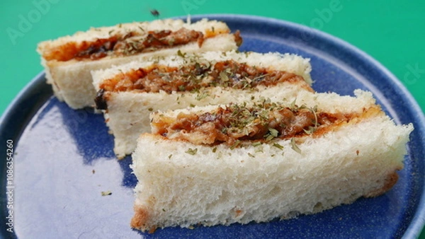 Obraz group of sliced ​​bread with meat filling, fried onions on a blue plate, green background