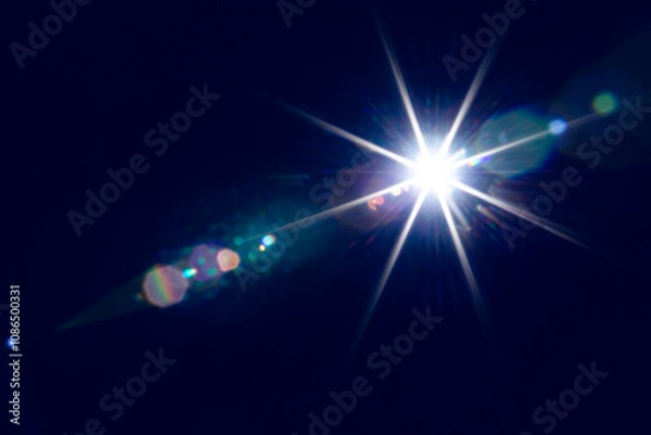 Fototapeta Bright shining light illuminating dark space with lens flare effects creating vivid star-like patterns in darkness.