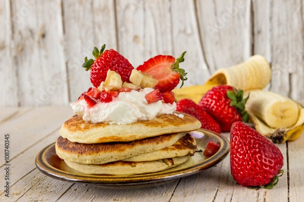 Obraz Блины с мороженным, клубникой и бананами для завтрака. Фон, текстура деревянный