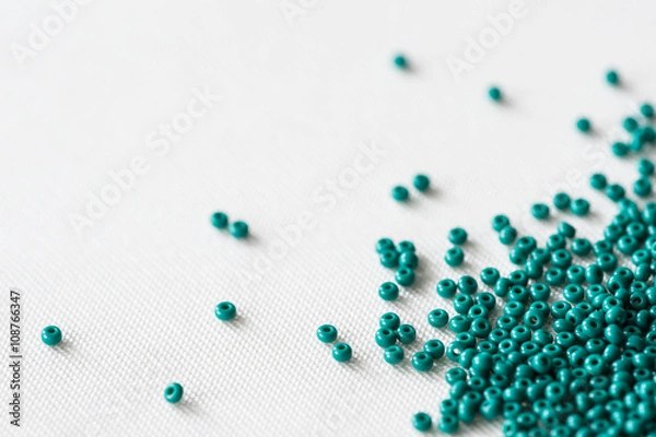 Fototapeta Scattered seed beads of emerald color on the textile background 