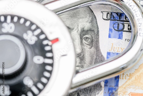 Fototapeta Financial or cyber security, fraud prevention, safeguarding assets and secure transactions : A combination of a US 100 dollar bill featuring Benjamin Franklin partially obscured by a combination lock.